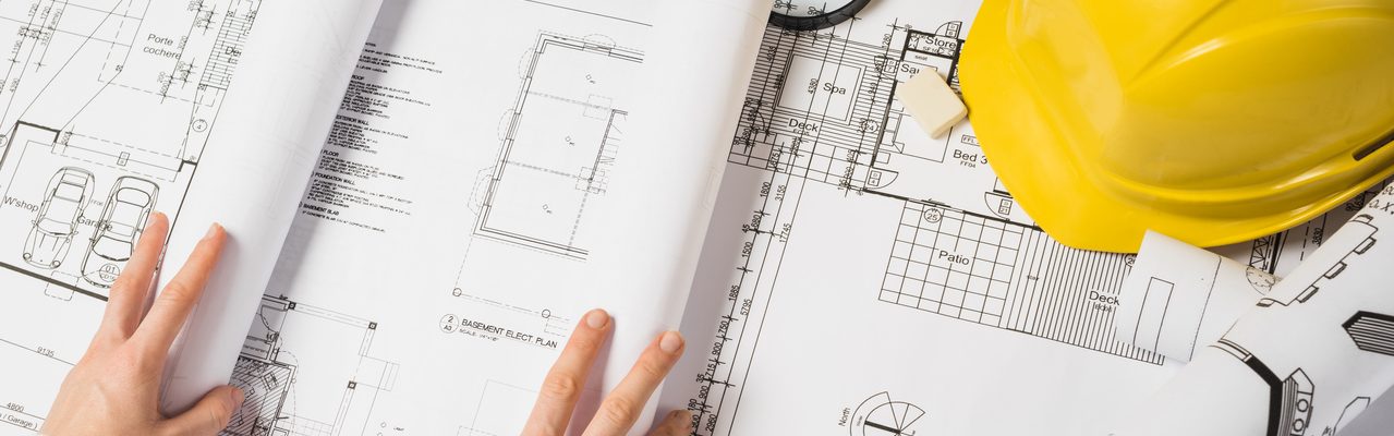 Les mains d'une personne sont posées sur un plan et un casque de chantier.